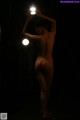 A nude woman standing in a dark room holding a light.