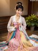 A woman in a pink and yellow hanbok sitting on the floor.