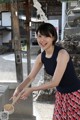 A woman in a blue top and red skirt holding a wooden spoon.