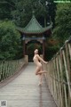 A naked woman standing on a wooden bridge.