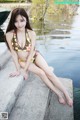 A woman in a bikini sitting on the edge of a lake.