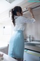 A woman in a white shirt and blue skirt standing in a kitchen.