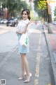 A woman in a white shirt and blue skirt is standing on the street.