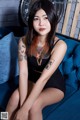 A woman sitting on a blue couch with a tattoo on her arm.