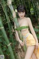 A woman in a yellow skirt posing in a bamboo forest.