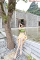 A woman in a green top and yellow skirt sitting on a stone wall.