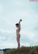 A woman in a blue bikini standing on a grassy hill.