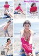 A woman in a pink bikini sitting on a surfboard on the beach.