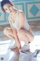 A woman in a white tank top and white sneakers crouching on the floor.