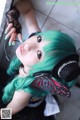 A woman with green hair wearing headphones and a butterfly mask.