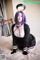 A woman with purple hair sitting on a bed.