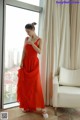 A woman in a red dress standing by a window.