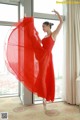 A woman in a red dress is dancing in front of a window.