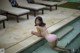 A woman in a pink bikini sitting on the edge of a pool.