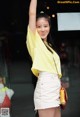 A woman in a yellow shirt and white skirt posing for a picture.