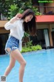 A woman in a white shirt and denim shorts dancing by a pool.