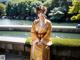 A woman in a yellow kimono standing next to a pond.