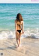 A woman in a black bikini walking on the beach.