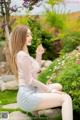 A woman sitting on a rock in a garden holding a flower.