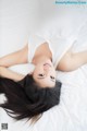 A woman laying on top of a bed wearing a white shirt.