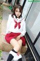 A woman in a school uniform sitting on a stone ledge.