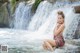 A woman sitting on a rock in front of a waterfall.