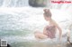 A woman sitting in the water near a waterfall.