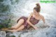 A woman in a pink dress sitting on a rock in the water.