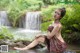 A woman sitting on a rock in front of a waterfall.