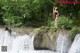 A woman standing on a rock in front of a waterfall.