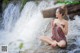 A woman sitting on a rock in front of a waterfall.