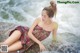 A woman sitting on a rock in the water.