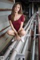 A woman in a red bodysuit sitting on a metal railing.