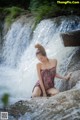 A woman sitting on a rock in front of a waterfall.