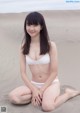 A woman in a white bikini sitting on a sandy beach.