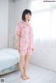 A woman standing in front of a bed wearing a pink pajamas.