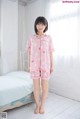 A woman standing in front of a bed wearing a pink pajama set.