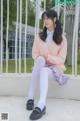 A young woman sitting on a white bench wearing white tights.