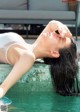 A woman in a white bathing suit laying on the edge of a pool.