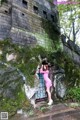 A woman in a pink dress standing in front of a stone wall.