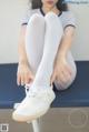 A woman sitting on top of a blue bench wearing white shoes.