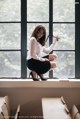 A woman sitting on a window sill holding a pair of scissors.