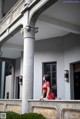 A woman in a red dress leaning against a column.