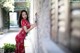 A woman in a red dress leaning against a wall.