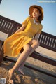 A woman in a yellow dress and hat sitting on a bench.