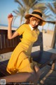 A woman in a yellow dress and hat sitting on a bench.