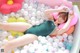 A woman laying in a bathtub filled with lots of balloons.